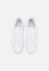 Zapatillas blancas hechas de material sintético suave, con punta redondeada, cierre con cordones y un logo sutil en el lado y en la plantilla.