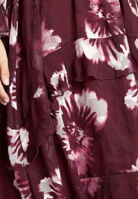 Abito floreale a strati di un profondo bordeaux, con motivi di fiori bianchi e rosa. Tessuto leggero con dettagli a volant e una sottile texture.
