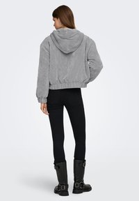 Hall halli korduroost lühike jope kapuutsi, elastse vöökohaga ja volüümikate varrukatega. Sobitatud mustade kitsaste teksade ja mustade saapadega.