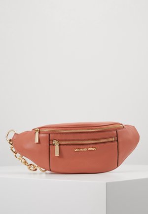 Rustfarvet læder Michael Kors hoftebæltetaske med guldfarvede lynlåse og kædedetalje, hvilende på en hvid overflade mod en lysegrå baggrund.