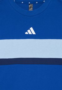 Blå bomulls t-skjorte med hvit Adidas-logo, horisontale lyseblå og marineblå striper over brystet, og rund hals.