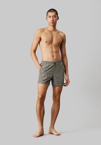 Costumi da bagno corti con un design a fantasia e vita con cordino, principalmente in tonalità di grigio e bianco, realizzati in un tessuto morbido e leggero.