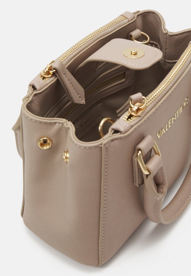 Sac à main beige clair avec une forme structurée, un matériau texturé, des finitions dorées, des fermetures éclair doubles et un intérieur doublé en tissu avec des compartiments.