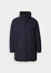 Giacca imbottita blu navy con colletto alto, tasche frontali e polsini elasticizzati. Tessuto liscio con un design minimalista e senza chiusure visibili.