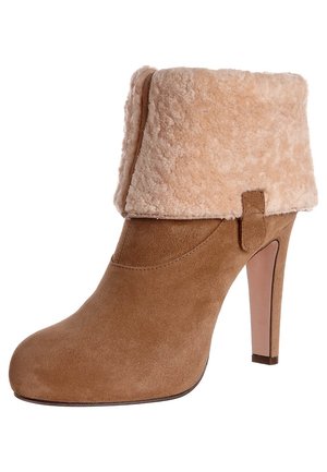 Zamszowy botek na wysokim obcasie w kolorze brązowym z założonym, jasno-beżowym mankietem z owczej skóry i zaokrąglonym noskiem, widziany z boku.