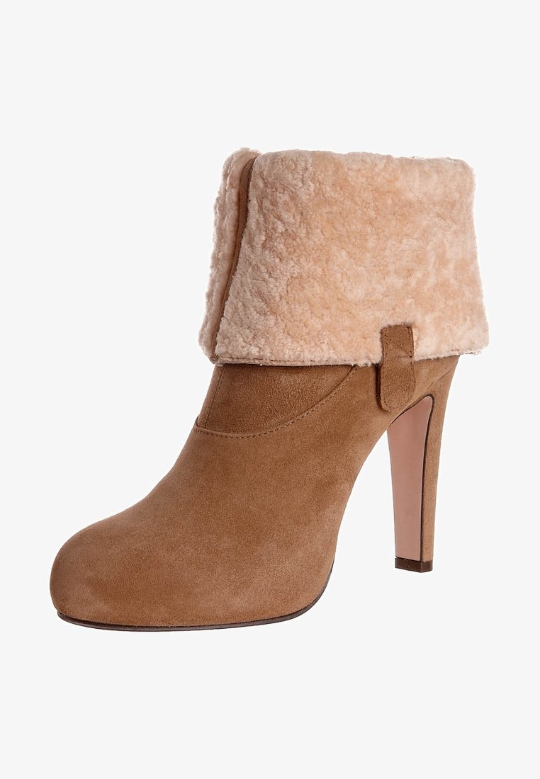 Bottine à talons hauts en daim fauve avec un revers en peau lainée beige clair plié et un bout rond, vue de profil.