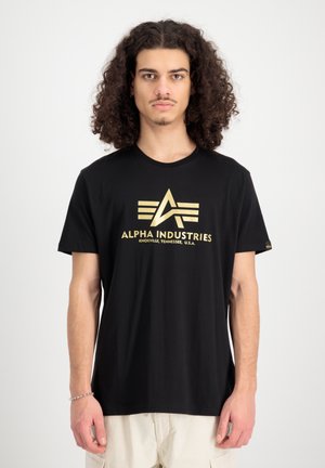 Schwarzes Baumwoll-T-Shirt mit einem goldenen Logo in einem geometrischen Design. Kurze Ärmel und klassischer Rundhalsausschnitt. Schlichte und entspannte Passform.