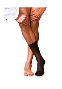Calzino marrone alla caviglia esposto su un piede accanto a un piede nudo; il calzino presenta una trama sottile e rigata. Lo sfondo è bianco uniforme.