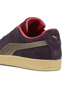 Puma suede tenisice u tamnoljubičastoj boji s bež gumenenim potplatom. Imaju teksturiranu stranu, ružičastu oblogu i zlatni logo na peti.