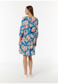 Blumenkleid mit drei Viertelärmeln, blauem Hintergrund, rosa und gelbem Blumenmuster, gestuftem Design, weichem Stoff, kombiniert mit weißen Sneakers.