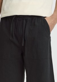 Sorte bomuldsbukser med en struktureret finish, elastisk talje, snøre og to forlommer.