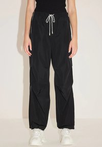 Zwarte, lichte trainingsbroek met een losse fit, elastische taille en koord. Bevat subtiele zijpanelen en gathered manchetten.