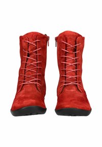 Un paio di stivali alla caviglia in suede rosso con lacci rosa e suole nere, visti frontalmente, con cerniere laterali su uno sfondo bianco.