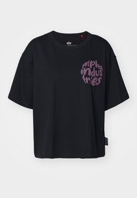 Camiseta de algodón negra con cuello redondo y corte oversize. Presenta un logo circular púrpura con las palabras "alpha industries" en la parte frontal.