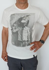 White cotton t-shirt featuring a graphic print of a suit with a globe for a head, holding a fuel can. The design uses grayscale tones.