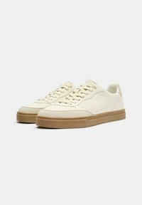 Cremfarbene Ledersneaker mit glatter Oberfläche, runder Spitze, flacher Gummisohle und strukturierten Schnürsenkeln. Minimalistisches Design, keine sichtbare Markenkennzeichnung.