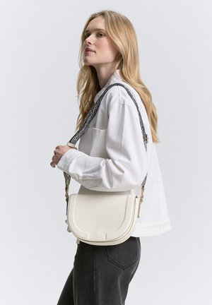 Borsa a tracolla bianca in pelle con flap curvo, cuciture dettagliate e una tracolla a motivo. La forma è minimalista e funzionale.