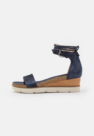 Sandalo wedge in suede blu navy con una fascia liscia sopra il piede e doppia cinghia alla caviglia con fibbia in metallo. Sottopiede in sughero testurizzato.