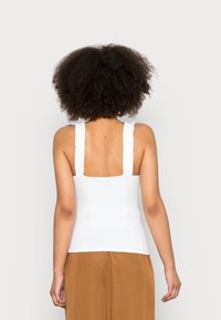 Top branco sem mangas com alças com volantes e um design ajustado. Textura suave com decote reto e uma forma clássica e simples.