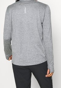 Langarm sportshirt van grijs gemêleerd materiaal, met een ronde hals en reflecterende witte strepen op de rug. Soepele textuur, ontspannen pasvorm.