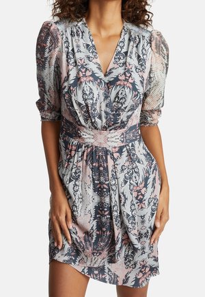 Woman wearing a knee-length, patterned dress with puffed sleeves and a cinched waist in muted pink, gray, and black colors.