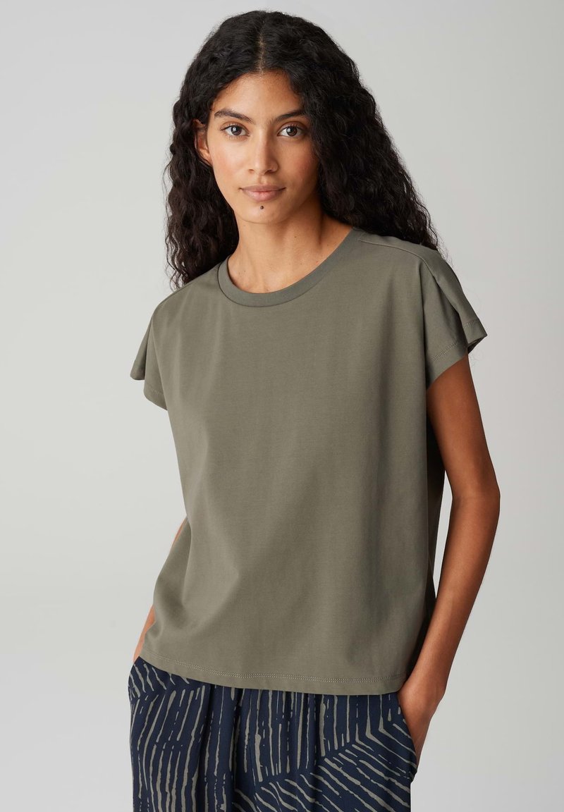 Koszulka z bawełny w oliwkowym kolorze, z krótkimi, podwiniętymi rękawami i okrągłym dekoltem. Miękka faktura, luźny krój, zestawiona z wzorzystymi granatowymi spodniami.