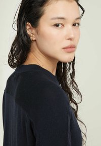 Maglione blu navy con una finitura testurizzata, caratterizzato da un colletto a coste e dettagli sulle spalle, abbinato a un semplice orecchino accentato.