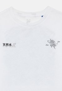 Λευκό T-shirt με στρογγυλή λαιμόκοψη, με ιαπωνικούς χαρακτήρες και το κείμενο «Peaceful Bliss» στο αριστερό στήθος, γραμμικό σχέδιο λουλουδιών και το κείμενο «Living Jewels» στο δεξί στήθος.