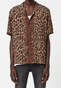 Camisa de manga corta con estampado de leopardo en tonos marrón, beige y negro, con cuello de campamento y cierre de botones en la parte delantera. Tejido ligero con un corte relajado.