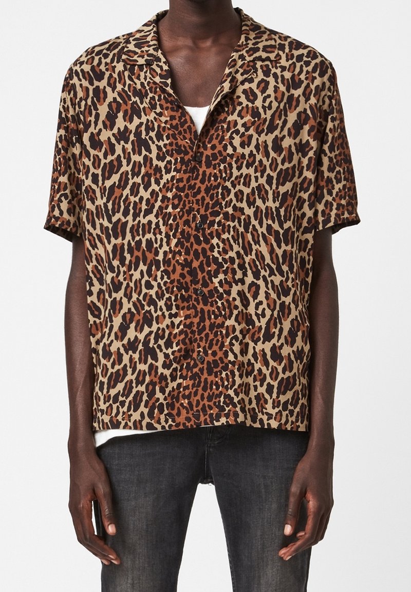 Camisa de manga corta con estampado de leopardo en tonos marrón, beige y negro, con cuello de campamento y cierre de botones en la parte delantera. Tejido ligero con un corte relajado.