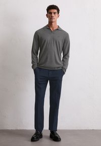 Szara polo z długim rękawem z kołnierzykiem, w parze z granatowymi spodniami i czarnymi butami. Slim fit z delikatnym logo na piersi.