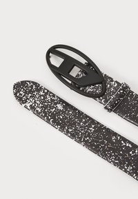 Ceinture en cuir noir et blanc à pois, dotée d'une élégante boucle ovale noire et d'une extrémité effilée pour l'ajustement. Surface texturée, design minimaliste.