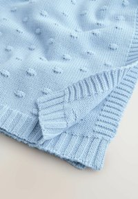 Svetlomodrá pletená látka s vystupujúcim vzorom bodiek a rebrovanými okrajmi, zložená tak, aby ukázala textúru a detaily stehu.