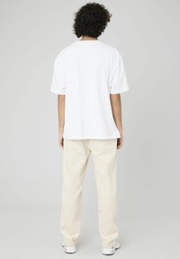 T-shirt blanc en coton avec une coupe décontractée, des manches courtes et un col rond, associé à un pantalon en velours côtelé de couleur crème.