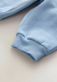 Niebieski mankiet bluzy bawełnianej z prążkowaną fakturą. Tkanina jest miękka i gładka, z delikatnym przeszyciem wzdłuż szwu.