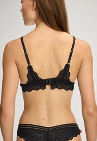 Sort blonder bralette med bølgekant, justerbare stropper og hægte lukning bagpå; delikat og detaljeret mønster over det hele.