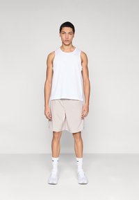 Valkoinen hihaton paita ja beigeä urheilushortsia, valmistettu kevyestä kankaasta, hienovaraisella logoyksityiskohdalla yhdistettynä valkoisiin lenkkareihin ja sukkiin.