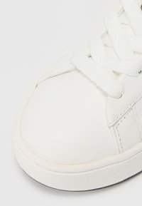 Hvit sneaker med en glatt læroverdel, rund tå og hvite snører. Har en teksturert gummisåle og subtile sømdetaljer.