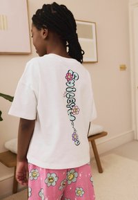 T-shirt en coton blanc avec une inscription "smiley" colorée et des motifs floraux au dos. Assorti à un short rose à motifs floraux.