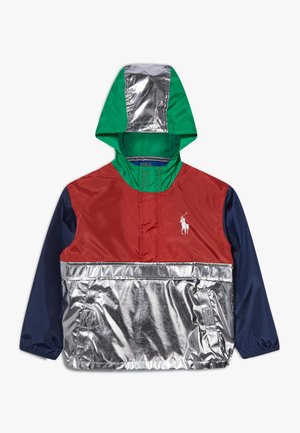 Dziecięca kurtka przeciwwiatrowa z kapturem w zielonym kolorze kaptura, czerwoną częścią na piersiach, granatowymi rękawami i odblaskowymi srebrnymi elementami na kapturze i u dołu.