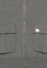 Gray zip-up hoodie made of soft fabric, featuring two front patch pockets and a metallic zipper. Includes a small metallic accent on the pocket.