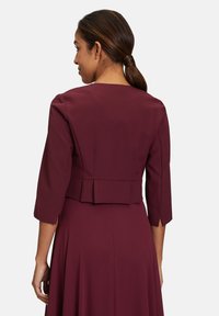 Bordeaux jurk met een aansluitende bustier en driekwart mouwen, met een geplooide rugontwerp en een gladde stoftextuur.