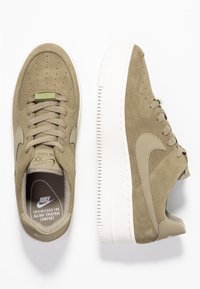 Zapatillas de ante verde oliva con diseño perforado, media suela blanca y cordones planos. Presentan el logo de Nike en la lengüeta y en la plantilla.