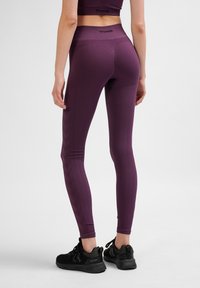 Lila högmidjade leggings med ribbad textur, smidigt material och logotypdetalj på midjebandet, kombinerat med svarta träningsskor.