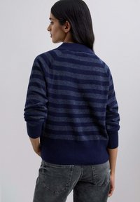 Navy striped sweater with a textured fabric, featuring horizontal stripes and a mock collar. The sleeves are slightly rolled up, paired with gray jeans.