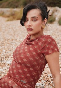 Rochie roșie în carouri, cu decolteu rotund și mâneci scurte, confecționată dintr-un material ușor cu texturi delicate țesute și o etichetă accentuată.