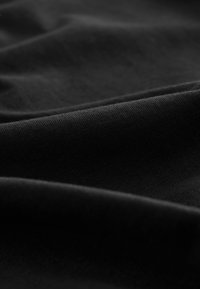 Tessuto nero con una trama liscia, che presenta leggere pieghe e grinze. Il materiale appare morbido ed elastico, ideale per l'abbigliamento.