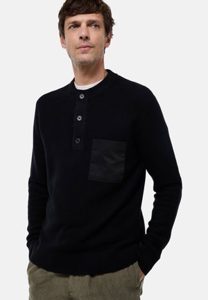 Pull en maille bleu marine foncé avec un col rond, une patte de boutonnage à quatre boutons et une poche plaquée noire mate sur la poitrine gauche. Tissu texturé.