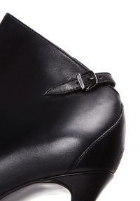 Zapato de tacón alto de cuero negro con punta afilada, silueta curvada y una combinación de superficies lisas y texturizadas con una correa de hebilla.