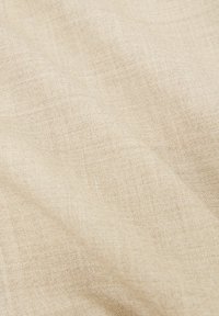 Tissu beige tissé avec une surface légèrement texturée et un motif de fibres naturelles visible, présenté en plis doux.